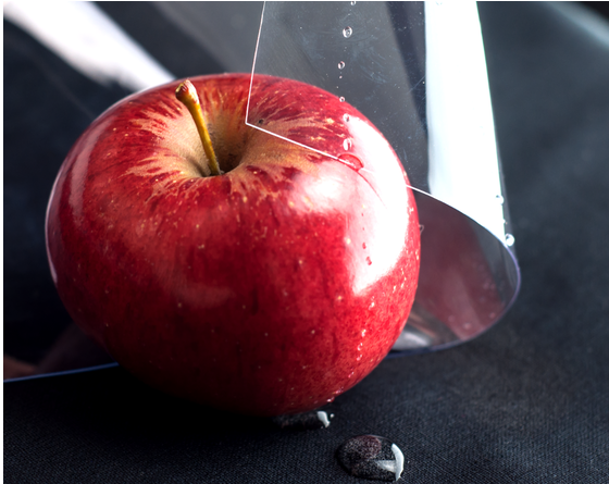 Un foglio lucido e trasparente di vinile in PVC che copre parzialmente una mela rossa con gocce d'acqua sulla sua superficie, dimostrando le sue proprietà di sicurezza alimentare.