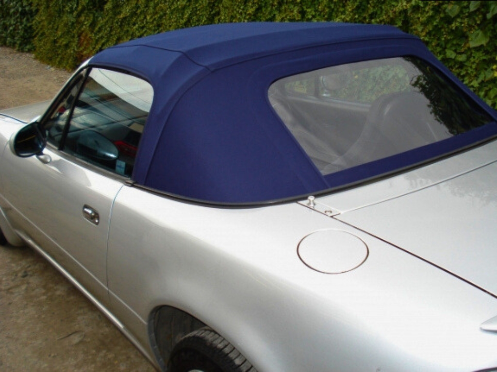 The back and side view of a silver convertible car with a dark blue soft top.