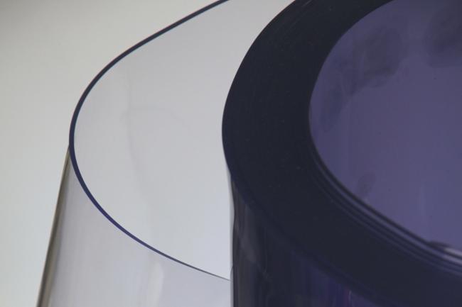 Un rollo grande de vinilo de PVC semitransparente con un sutil tinte azul, parcialmente desenrollado para revelar su material liso y flexible.
