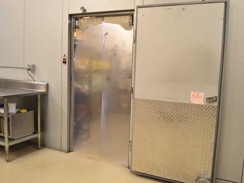 Cold storage room with transparent swing pvc doors beside metal entry door.