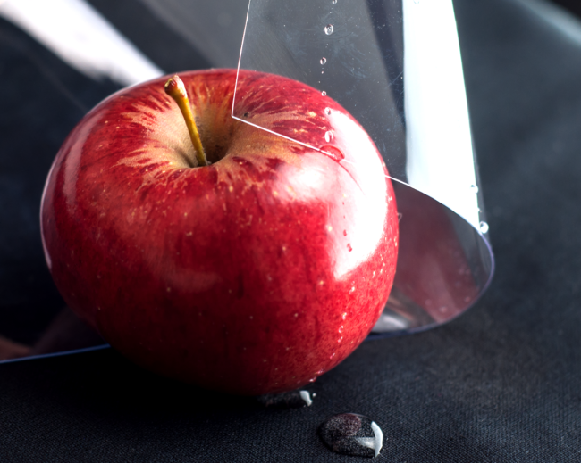 Un foglio lucido e trasparente di vinile in PVC che copre parzialmente una mela rossa con gocce d'acqua sulla sua superficie, dimostrando le sue proprietà di sicurezza alimentare.