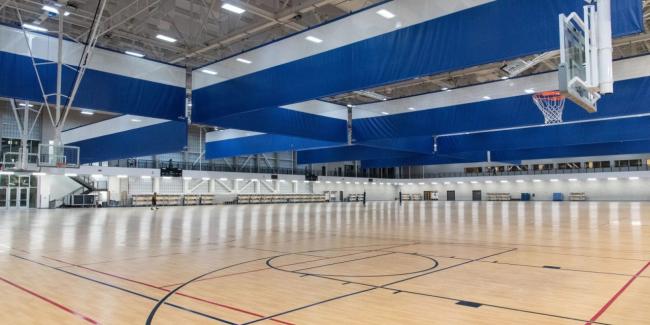 large indoor gymnasium with retractable blue and white vinyl divider curtains hanging from the ceiling to separate sports courts