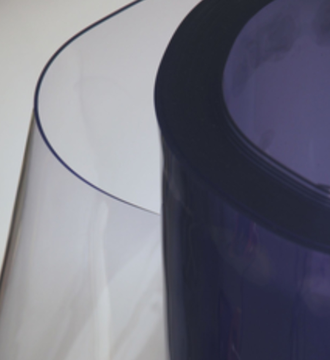 Un grand rouleau de vinyle PVC semi-transparent avec une légère teinte bleutée, partiellement déroulé pour révéler son matériau lisse et flexible.