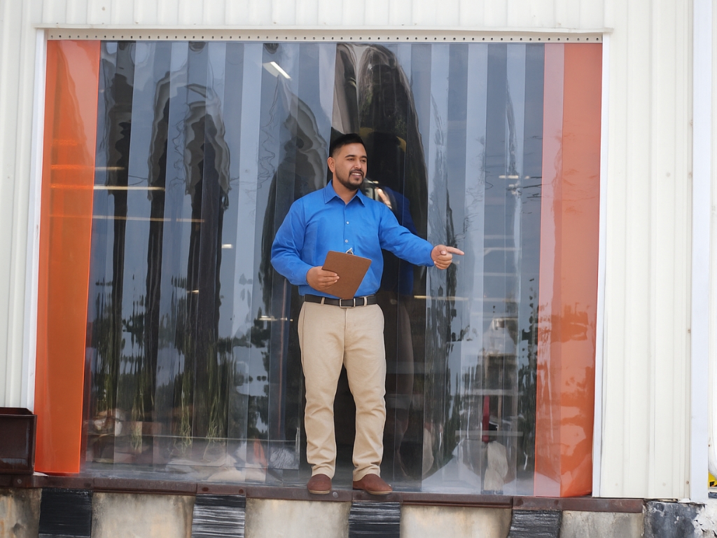 A man points outside a warehouse through a PVC strip curtain.