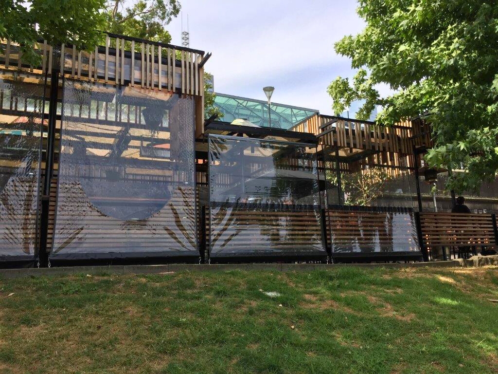 An outdoor patio or structure with a combination of wood paneling and large clear vinyl screens hanging between the supports, providing an enclosure.