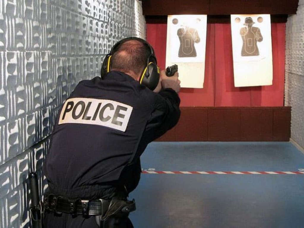 Police officer practicing shooting at paper targets in an indoor range.