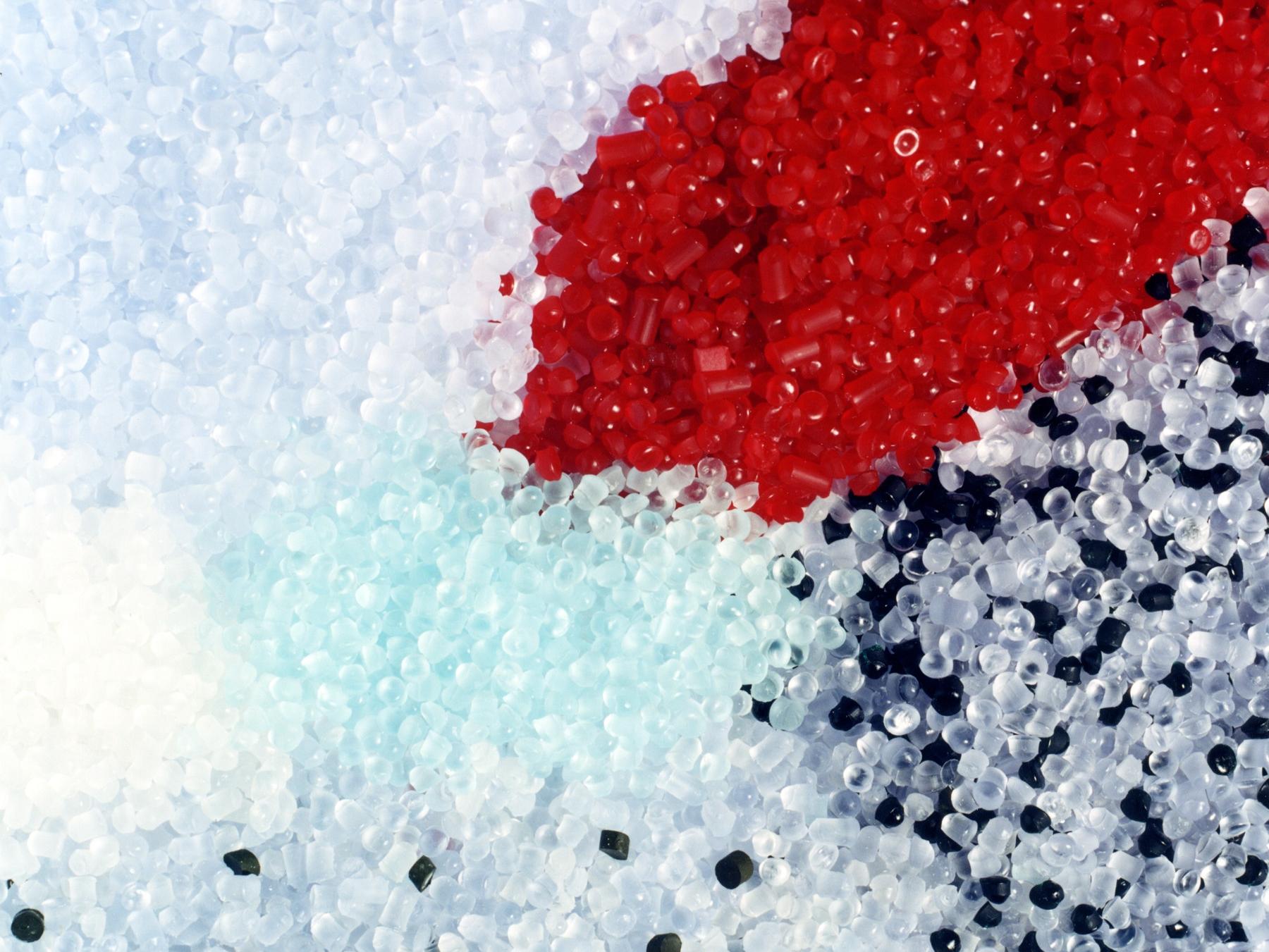close-up of multicolored PVC pellets in red, white, blue, and black, used as raw material in plastic manufacturing