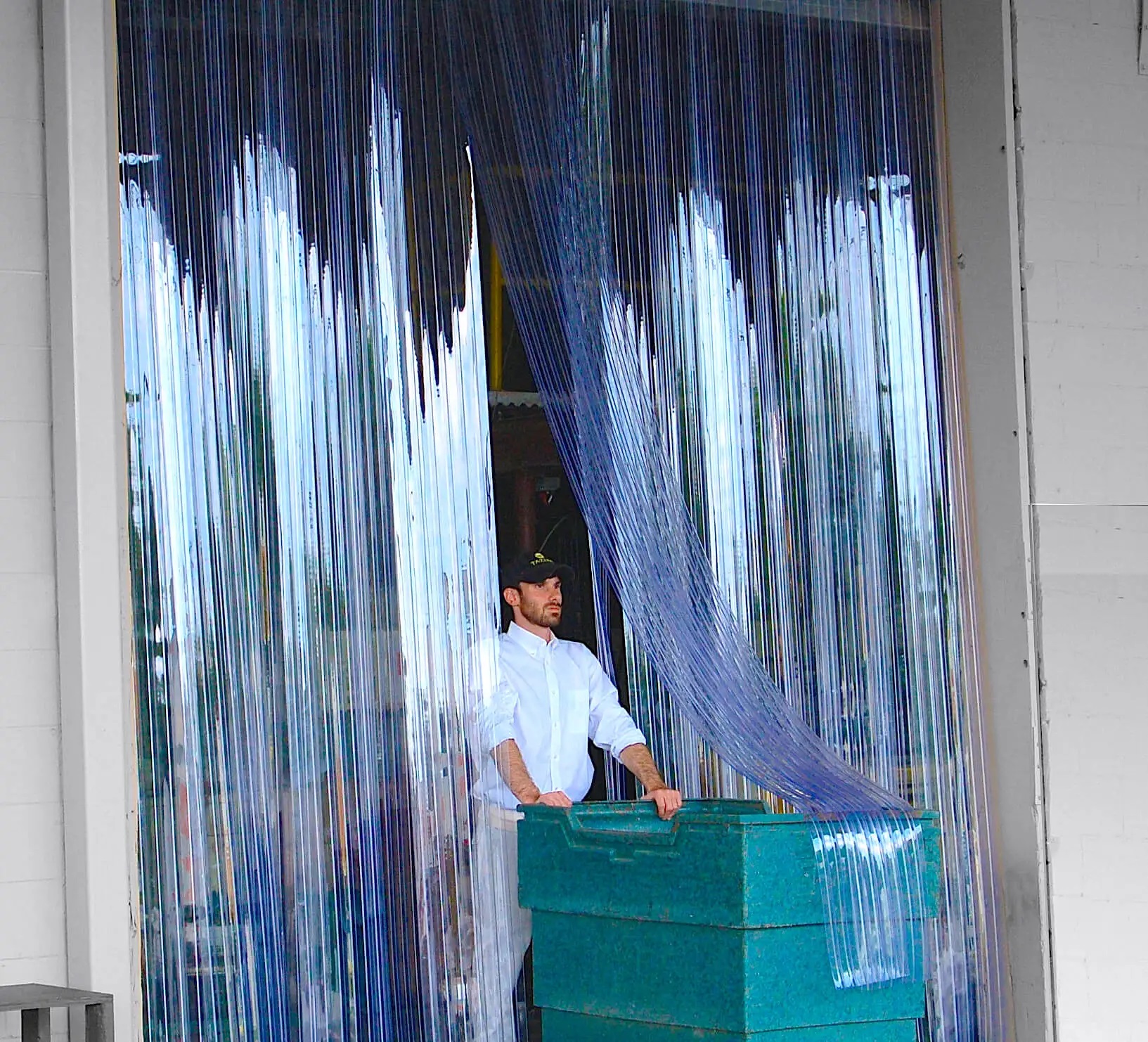 man pushing a green insulated cart through a doorway with clear ribbed PVC strip curtains, used for temperature control and hygiene in industrial settings