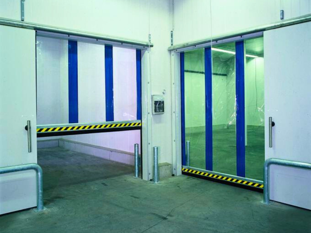 Two adjacent cold storage doors are partially open. Both doors have clear plastic panels with bold vertical blue stripes and black and yellow warning stripes along the bottom.