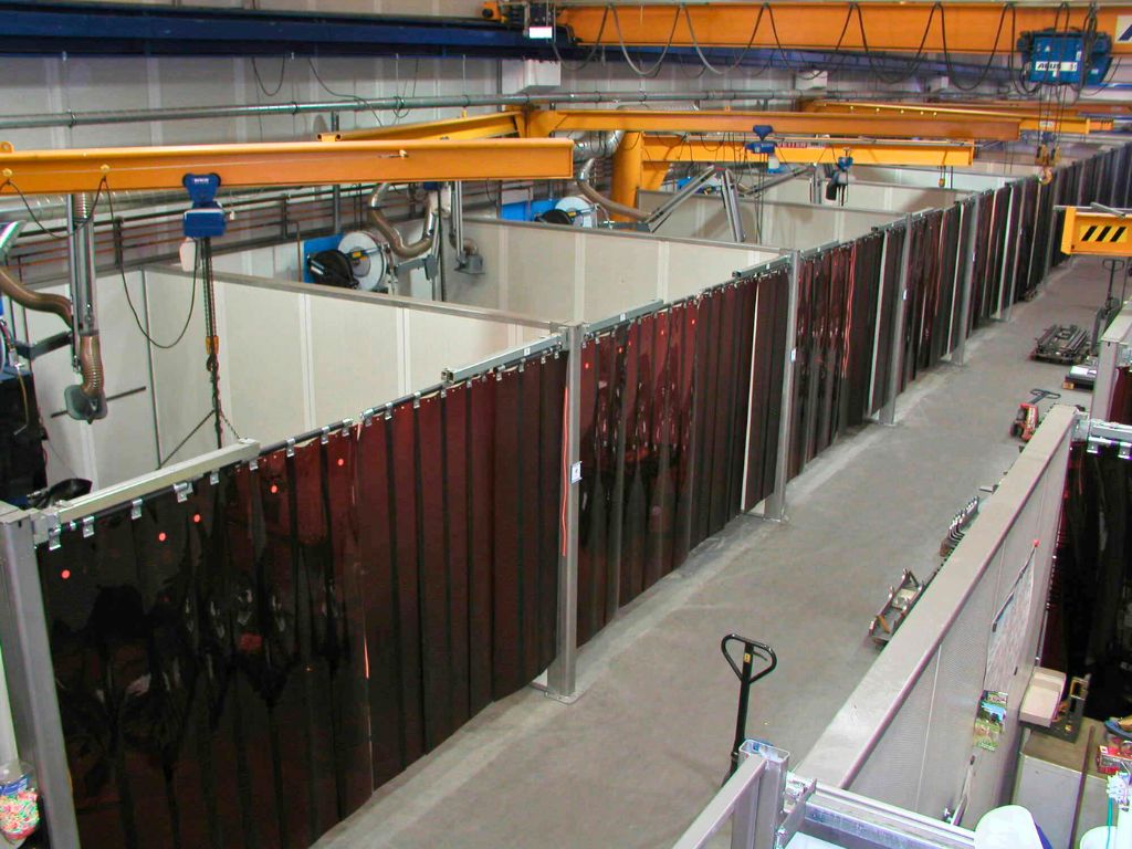 Industrial workshop with multiple welding booths separated by dark strip curtains.