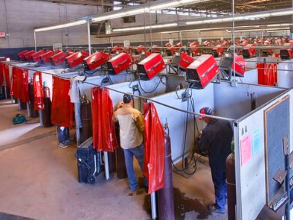 Large welding training facility with rows of red curtain booths and equipment.