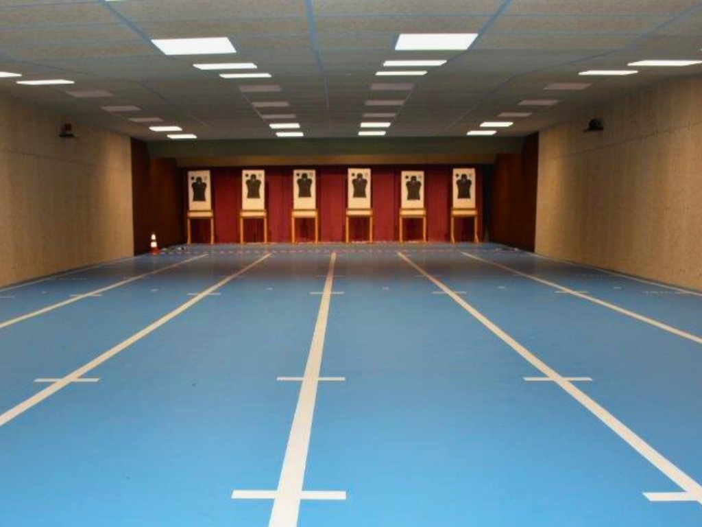 Wide indoor shooting range with blue lanes and silhouette targets at the end.