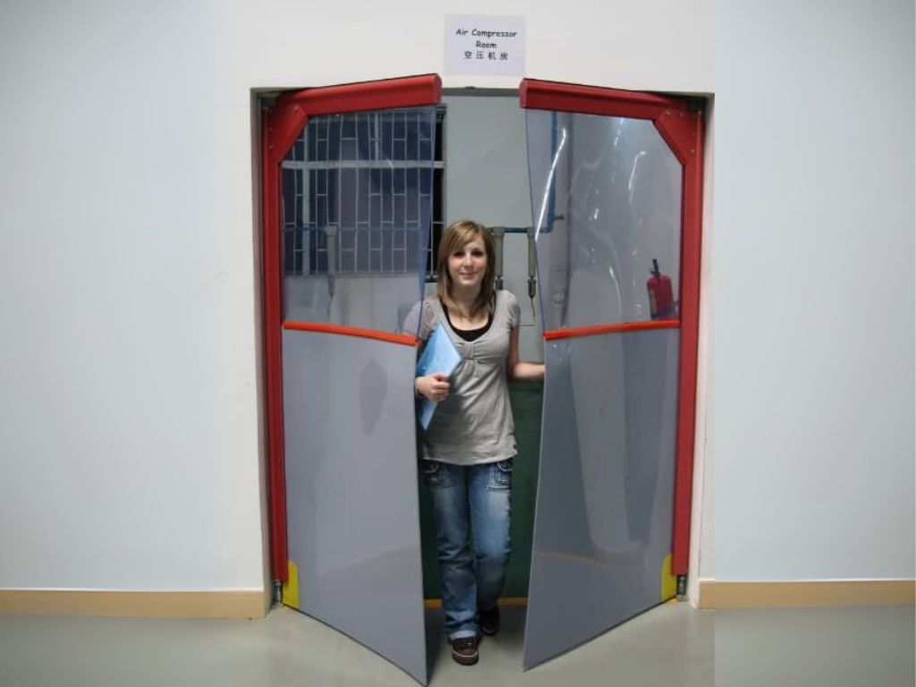 Woman walking through a swing door with transparent pvc panels and red frame.