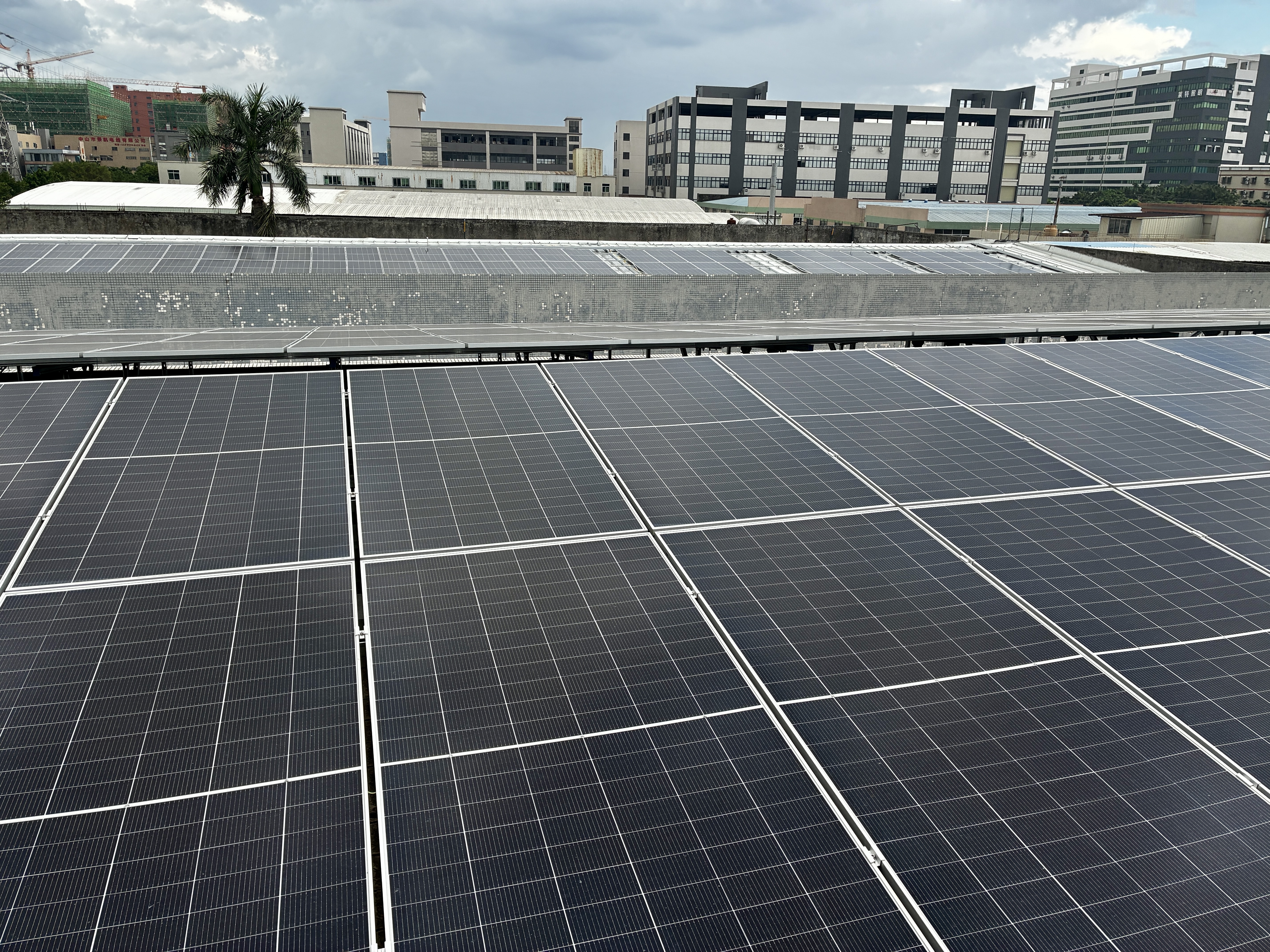 A wide view of rooftop solar panels installed on Zhongshan Extruflex building, with modern factory buildings and a cloudy sky in the background.
