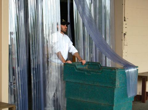 A man pushing a blue green cart passing through pvc strip curtains