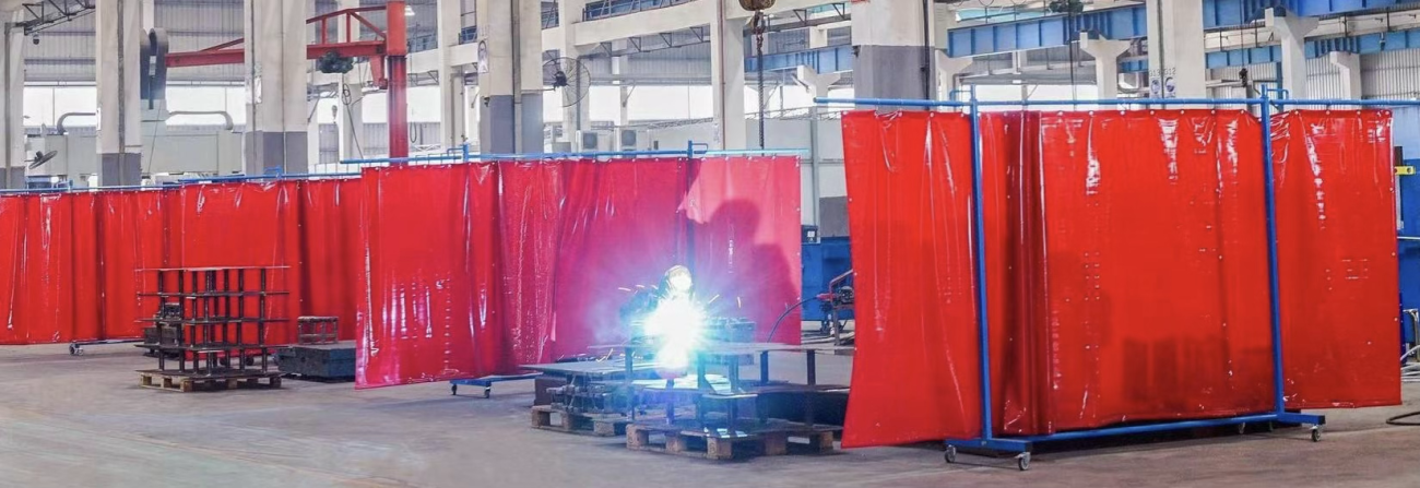 Soudeur travaillant derrière des rideaux rouges en PVC Screenflex dans un environnement industriel, avec plusieurs cloisons mobiles