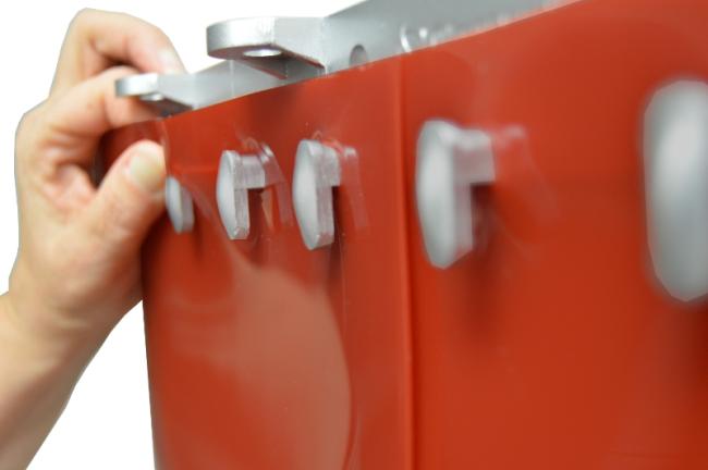 Un primer plano de la mano de una persona instalando un panel de vinilo transparente en un soporte de montaje rojo utilizando herrajes QuickMount, con sujetadores en forma de gancho para una fácil fijación.