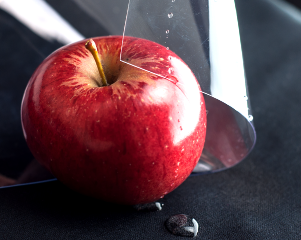  A glossy, transparent sheet of PVC vinyl partially covering a red apple with water droplets on its surface, demonstrating its food-safe properties.